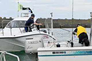 A coast guard officer (left) handing out awareness leaflets using a landing net to people enjoying fishing at sea