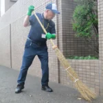 マンションに面した道路をほうきでてきぱきとはく伊藤喜春さん