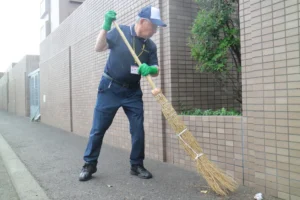 マンションに面した道路をほうきでてきぱきとはく伊藤喜春さん