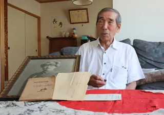 Mr. Kikuo Sakaguchi speaks about his hopes for peace in front of photographs and belongings of his father, Fukumatsu.