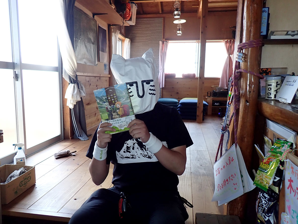 漫画「今日からはじめる山登り」を手にポーズを取るじゅごん大輔さん＝４月２７日、表丹沢の木ノ又小屋