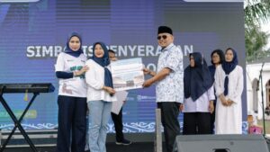 Bupati Simalungun, Anton Achmad Saragih (kanan) didampingi Weni Mega Sari, Pemimpin Cabang PNM Pematangsiantar (kiri), menyerahkan hadiah umroh kepada nasabah PNM.