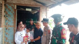 Camat Nurchinta Depi Tambunan menggendong bayi didampingi Wakapolsek Tanjung Beringin Iptu Zulfan Ahmad, personel Koramil 11/TB Sertu Budi Santoso dan Kepala Desa Mangga Dua, Budi Santoso di rumah warga yang terdampak banjir di Dusun IV Kebun Sayur, Desa Mangga Dua.