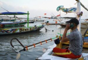 Nelayan Muncar, Banyuwangi tengah berkomunikasi menggunakan smartphone ditengah kesibukannya mencari ikan.
