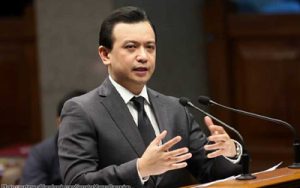 Man in a dark suit delivering a speech at a podium with two microphones in a formal indoor setting.