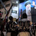 Bakhtiari nomads, wearing traditional dress, hold their guns during a pro-government gathering near the residence where former Iranian Supreme Leader Ayatollah Ali Khamenei, shown on a banner, was killed in U.S. and Israeli strikes on Feb. 28, in Tehran, Iran, May 18, 2026. (AP Photo/Vahid Salemi)