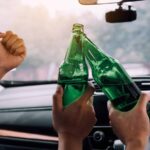 Celebrating with cheers and clinking green glass bottles inside a car during a festive occasion.