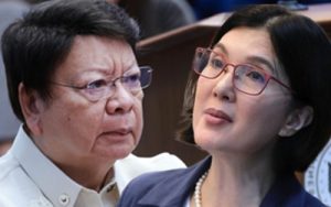 Two women in a conference room: an older woman with short dark hair and glasses, and a younger woman with dark hair and red glasses, looking attentive.