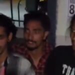 A young group of men standing together outdoors at night, engaging in conversation.