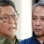 Two men engaged in a serious conversation, one wearing a green shirt and glasses, the other in a blue shirt with gray hair.