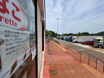 Large trucks are parked outside a 7-Eleven convenience store at the Ozumi Parking Area on the Hokuriku Expressway in Nagaoka, Niigata Prefecture, on May 27, 2026. A sign on the left invites people to come inside and cool off. (Mainichi/Nami Hamada)