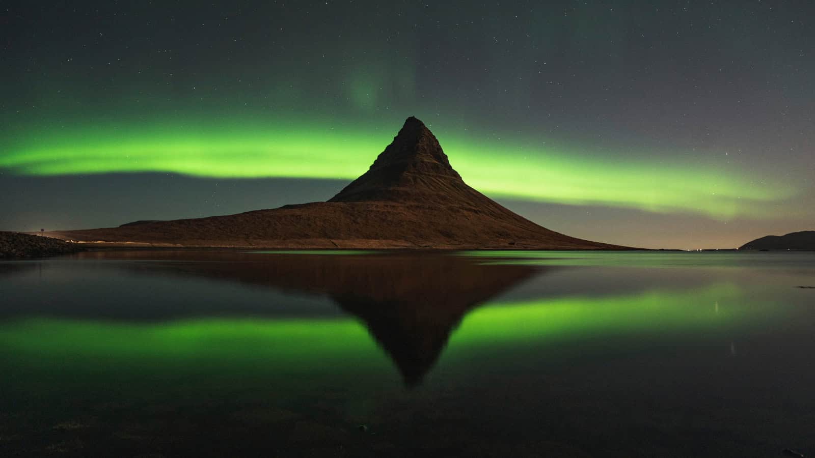 Aurora Borealis over Kirkjufell mountain in Iceland at night, reflecting on calm water.