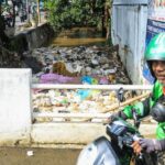 Warga melintas di dekat aliran sungai yang dipenuhi sampah di kawasan Limo, Depok, Jawa Barat, Senin (4/5/2026).