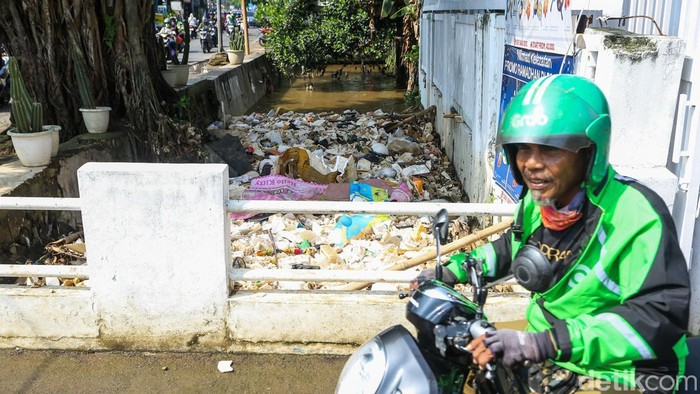 Warga melintas di dekat aliran sungai yang dipenuhi sampah di kawasan Limo, Depok, Jawa Barat, Senin (4/5/2026).