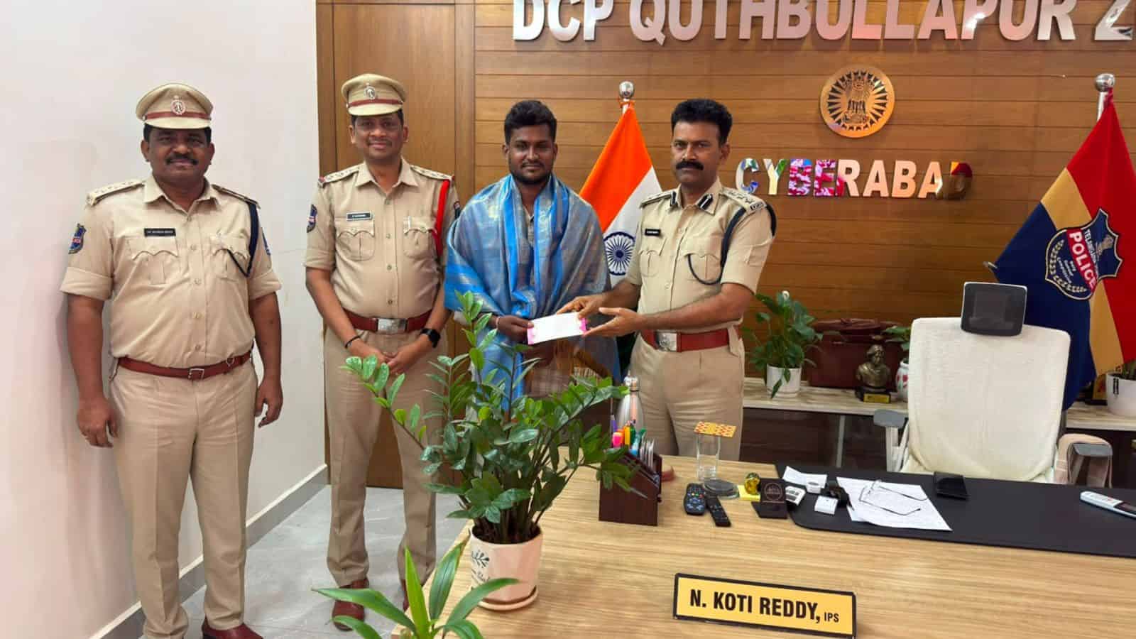 A man receiving an award from police officers in an office setting with flags and a wooden wall backgroun.